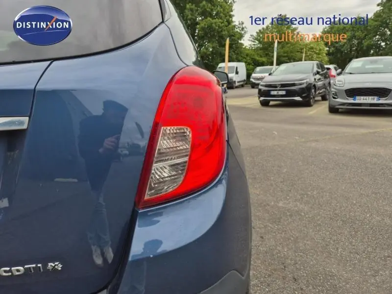 Gros plan sur le feu arrière droit d'un Opel Mokka bleu outremer, avec logo CDTI et parking en arrière-plan.