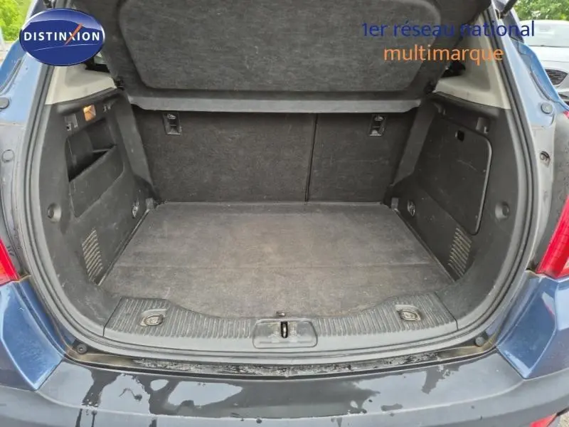 Coffre ouvert vu de l'arrière d'un Opel Mokka bleu outremer, montrant l'espace de chargement et le cache-bagages relevé.