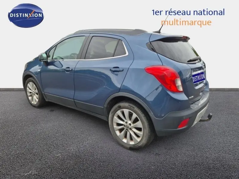 Opel Mokka bleu outremer vue 3/4 arrière droit avec jantes alu et barres de toit visibles.