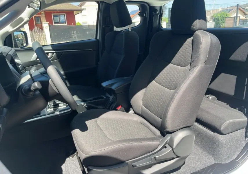 Vue intérieure côté conducteur de l'Isuzu D-MAX 2.2 TD 164 Space Evolution avec sièges tissu gris et accoudoir central.