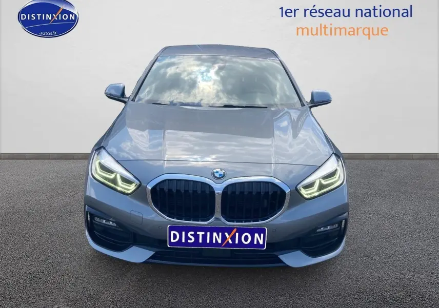 BMW Série 1 gris foncé vue de face, phares LED allumés et calandre double haricot distinctive bien visible.