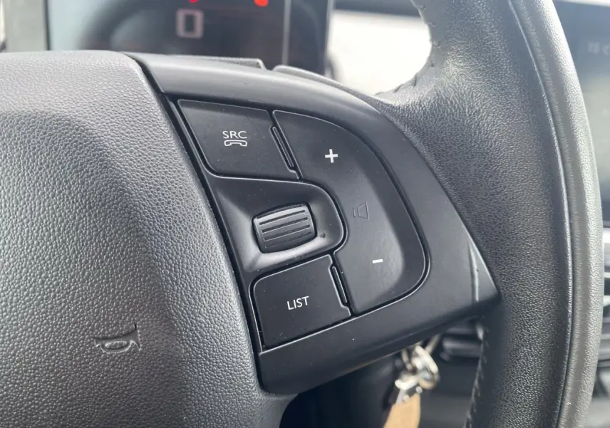 Gros plan sur les commandes gauche du volant noir du Citroën C4 Cactus 2015 essence blanc, intérieur moderne.