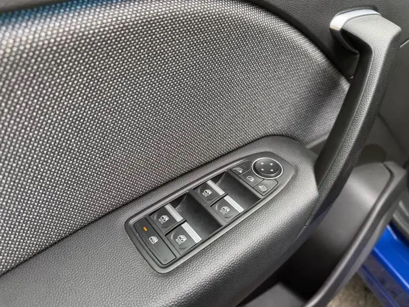 Gros plan sur la commande des vitres électriques côté conducteur du Renault Captur 2025 Bleu Iron avec tissu gris et poignée noire.