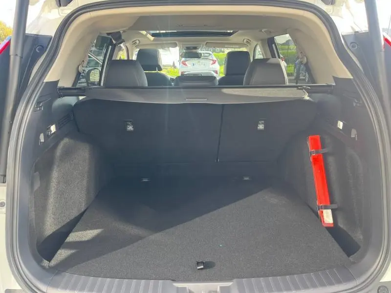Coffre ouvert du Honda CR-V 2024 blanc, vue arrière avec banquette noire et triangle de sécurité rouge fixé à droite.