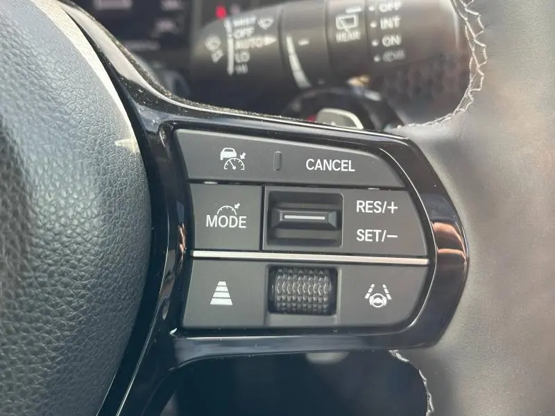 Gros plan sur les commandes noires du volant cuir du Honda CR-V 2024 hybride, avec régulateur de vitesse adaptatif.