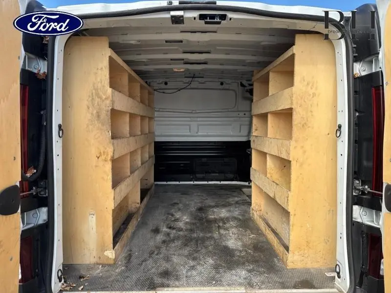 Vue arrière intérieure du fourgon blanc avec aménagements en bois sur les côtés pour rangement.