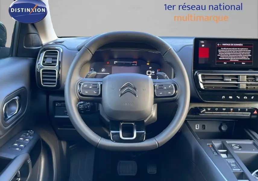 Vue frontale du poste de conduite du Citroën C5 Aircross 2025, volant cuir noir et écran tactile central allumé.