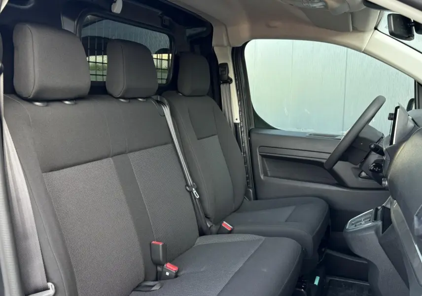 Vue intérieure côté conducteur du Citroën Jumpy gris, montrant les sièges avant et la cloison vitrée isolante derrière.
