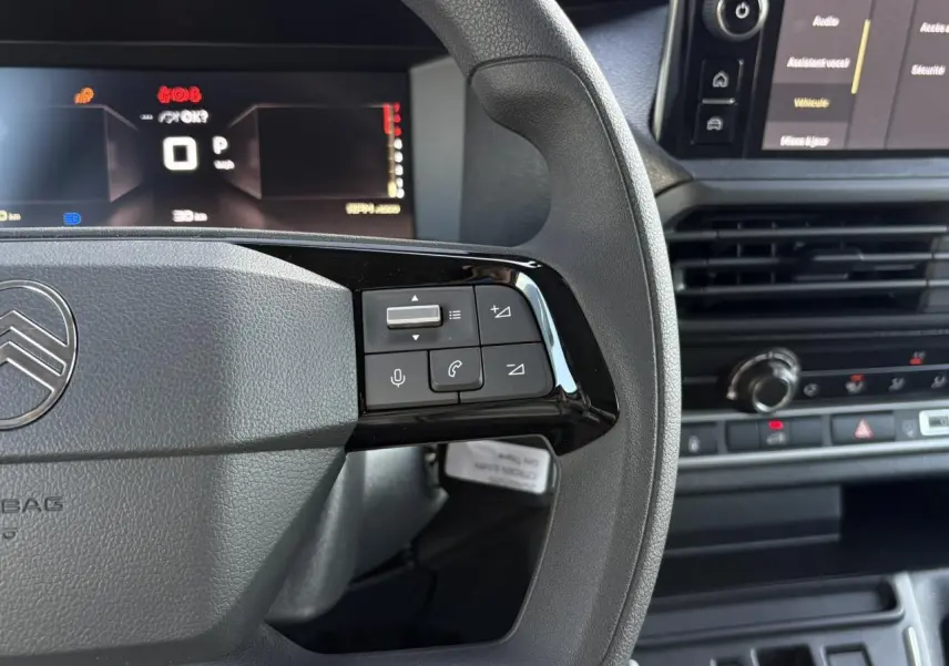 Gros plan sur le volant gris du Citroën Jumpy 2025, avec commandes audio et écran digital en arrière-plan.