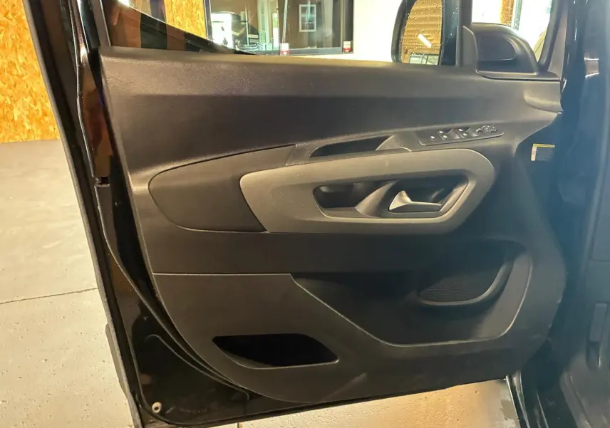 Vue rapprochée de la porte avant gauche noire du Citroën Berlingo 2020, montrant les commandes de vitres et la poignée intérieure.