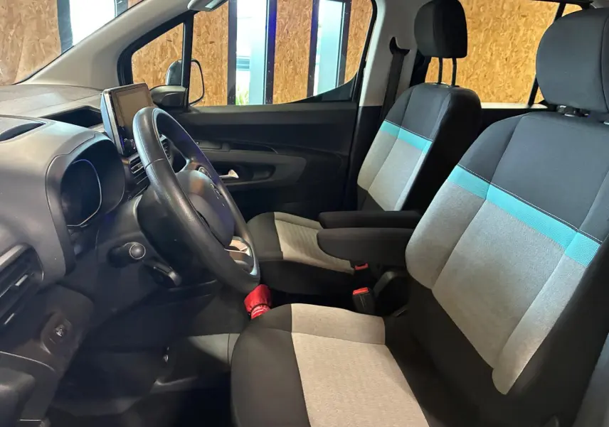 Vue intérieure côté conducteur du Citroën Berlingo noir 2020, sièges tissu gris et bleu avec volant et écran tactile.