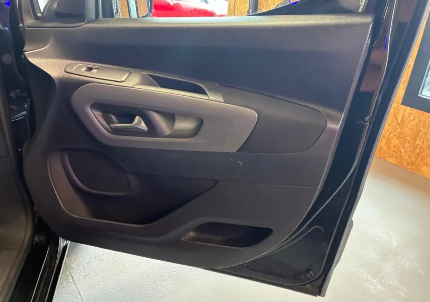 Vue intérieure de la porte avant gauche noire du Citroën Berlingo 2020, montrant la poignée et les commandes.