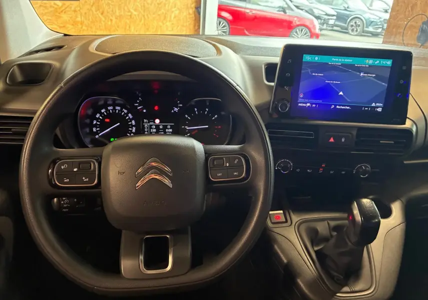 Vue intérieure centrée sur le volant et le tableau de bord du Citroën Berlingo noir avec écran tactile et levier de vitesses manuel.