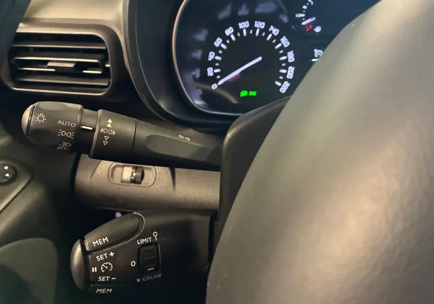 Gros plan sur le volant et les commandes de régulateur de vitesse d’un Citroën Berlingo noir, tableau de bord en arrière-plan.