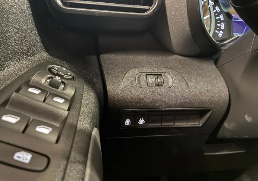 Détail intérieur côté gauche du tableau de bord noir du Citroën Berlingo 2020 avec commandes de vitres et réglage phares.