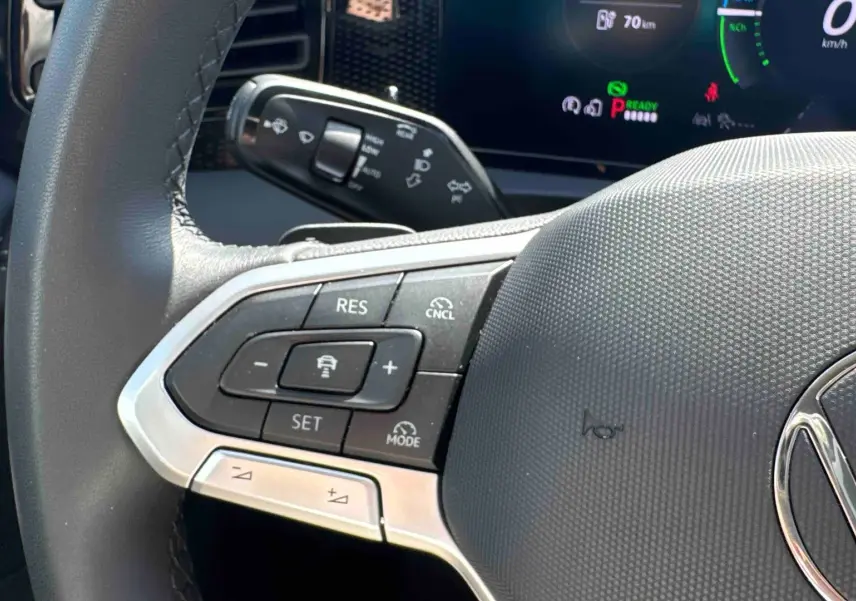 Gros plan sur le volant noir du Volkswagen Tiguan eHybrid 2025, montrant les commandes de régulateur de vitesse à gauche.