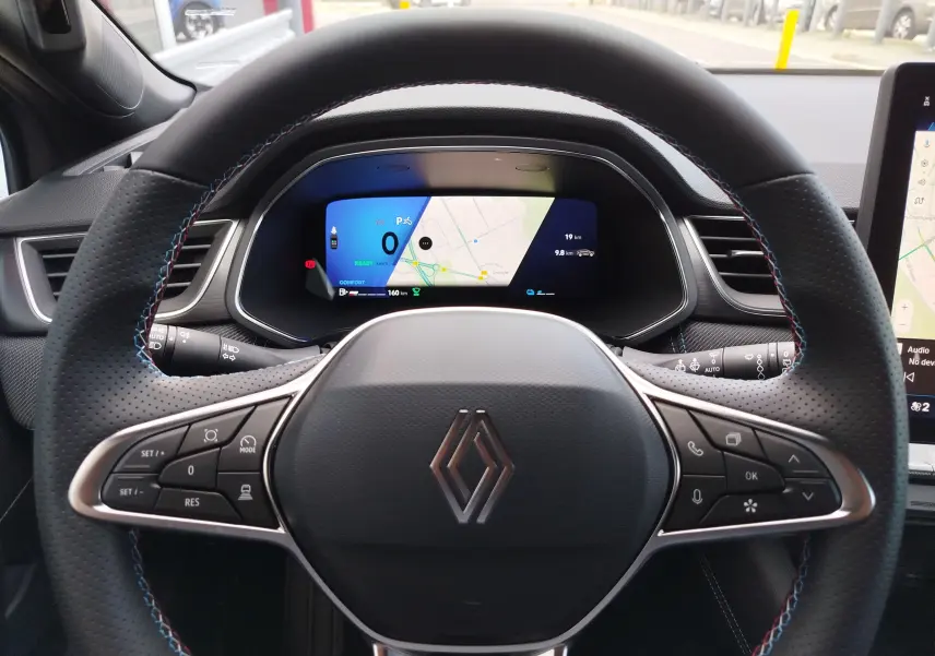 Vue centrée sur le volant perforé noir avec surpiqûres bleues et tableau de bord numérique du Renault Symbioz gris Cassiopée.
