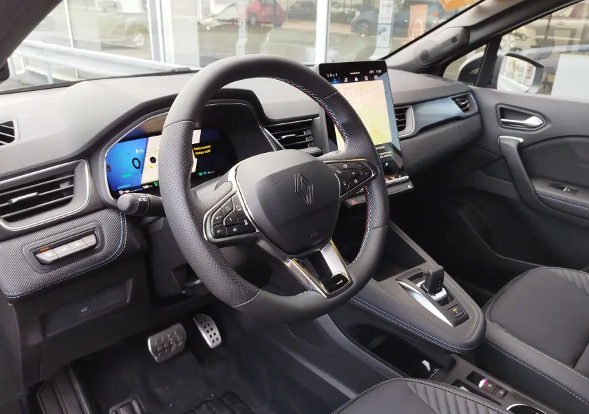Vue intérieure côté conducteur du Renault Symbioz gris cassiopée, volant cuir avec surpiqûres bleues et écran tactile central.