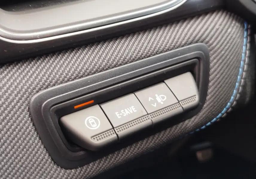 Gros plan sur les boutons de commande E-SAVE et réglage des phares, habillage carbone avec surpiqûres bleues, intérieur Renault Symbioz.