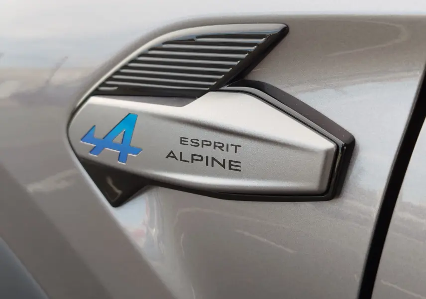 Gros plan sur l’insigne Esprit Alpine bleu et noir sur la carrosserie gris cassiopée métal d’une Renault Symbioz.