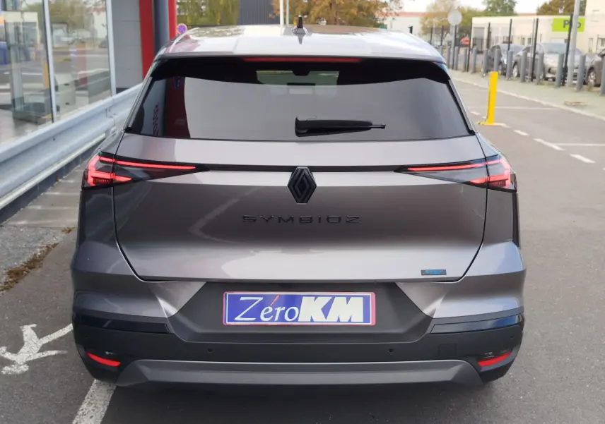Vue arrière d'une Renault SYMBIOZ gris cassiopée métallisé avec feux LED fins et logo central noir sur parking urbain.