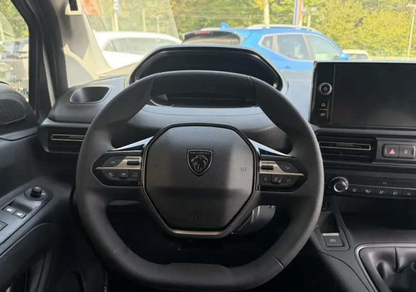 Vue intérieure centrée sur le volant cuir multifonctions du Peugeot Partner blanc avec tableau de bord et écran tactile.
