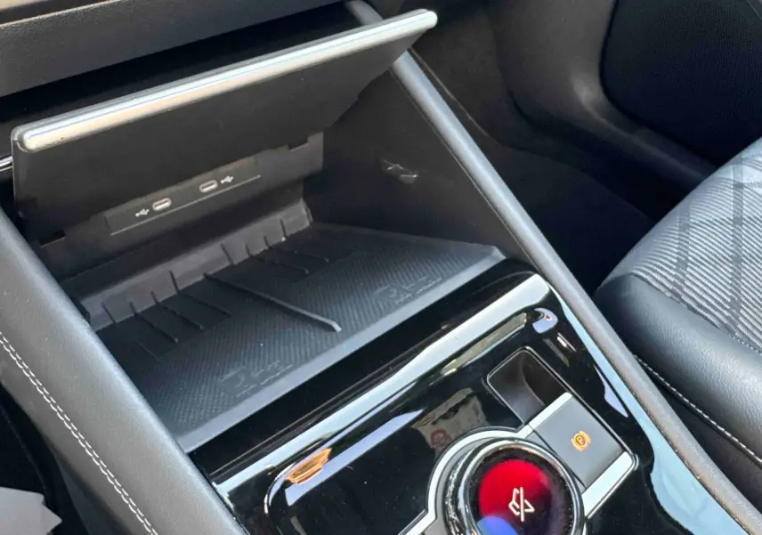 Gros plan sur la console centrale noire brillante du Volkswagen Tiguan 2025 avec chargeur sans fil et frein de stationnement électronique.