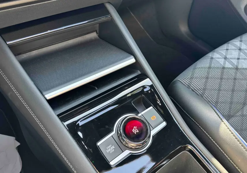 Vue rapprochée de la console centrale noire brillante avec bouton rotatif et siège avant gris à motifs du Volkswagen Tiguan 2025.