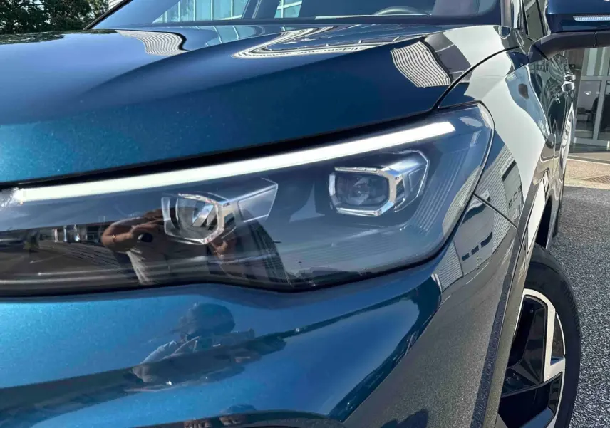 Gros plan sur le phare avant droit et la jante alliage 19 pouces d’un Volkswagen Tiguan bleu métallisé.