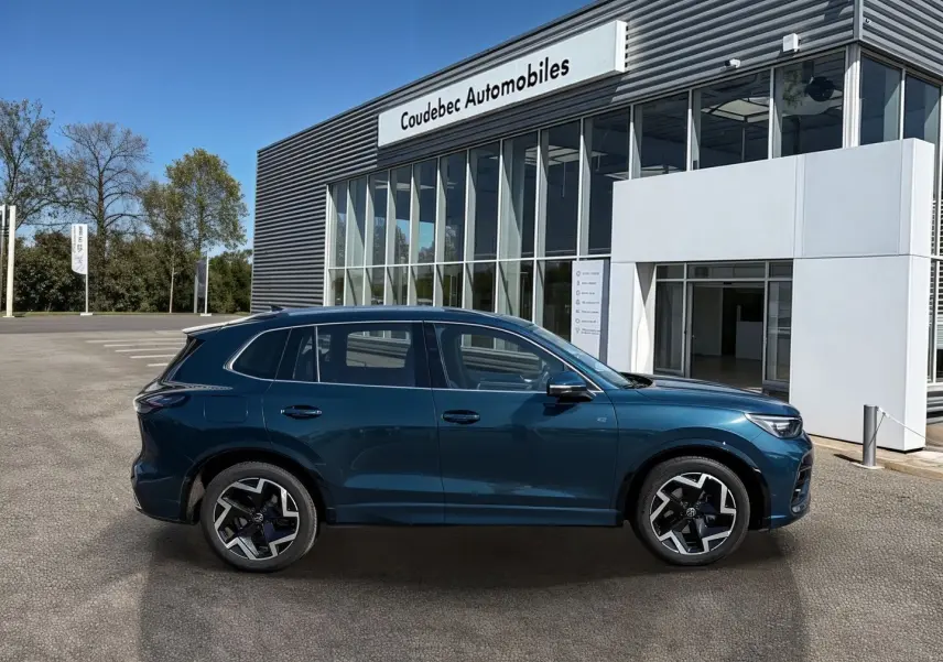 Vue de profil côté gauche d'un Volkswagen Tiguan 2025 bleu, avec jantes alliage 19 pouces et finition R-Line devant un concessionnaire.