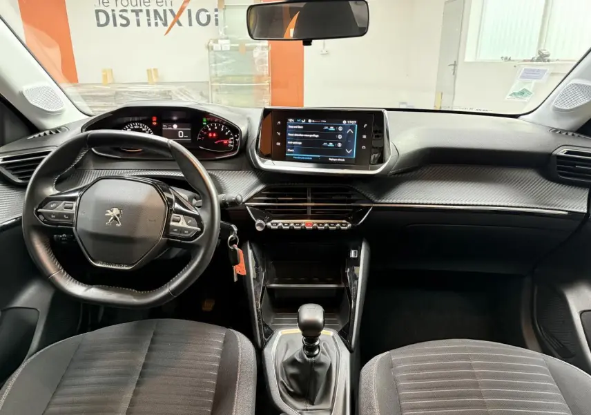 Vue intérieure avant de la Peugeot 208 2020 avec tableau de bord noir, volant multifonction et écran tactile central.