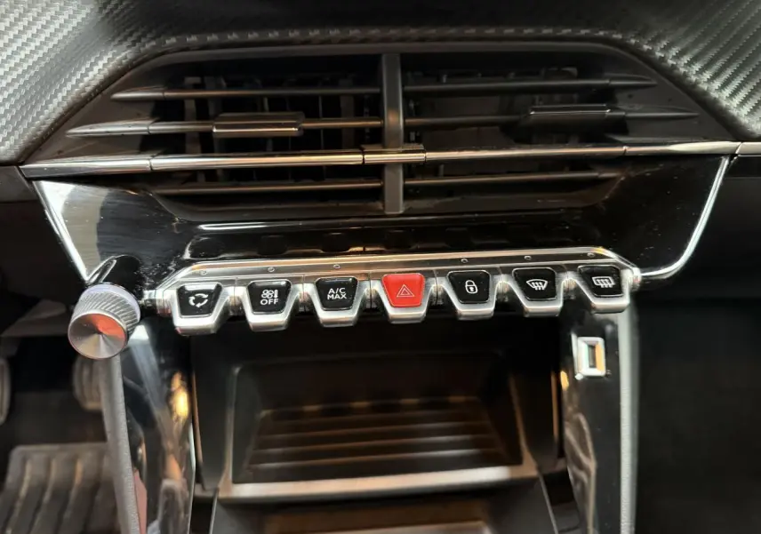 Gros plan sur la rangée de boutons de commande sous la ventilation du tableau de bord d'une Peugeot 208 jaune clair.