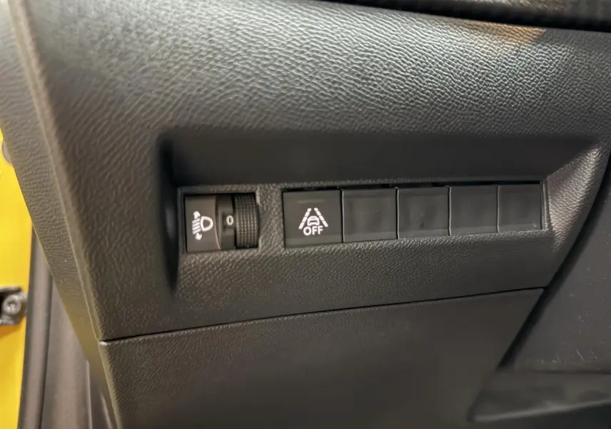 Gros plan sur les commandes de réglage des phares et de l'alerte de franchissement de ligne dans une Peugeot 208 jaune clair.