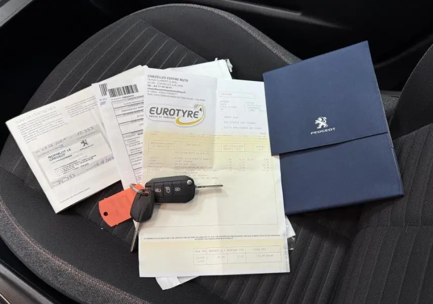 Vue rapprochée de la banquette arrière noire d'une Peugeot 208 avec clés, documents et carnet d'entretien posés dessus.
