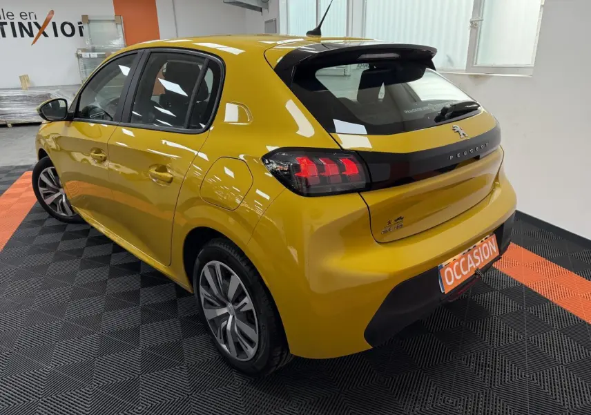Vue 3/4 arrière droite d'une Peugeot 208 jaune clair avec feux arrière à griffes et jantes alliage modernes.