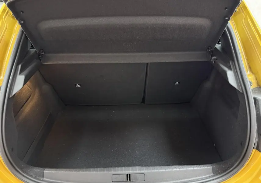 Coffre ouvert vu de l'arrière d'une Peugeot 208 jaune clair, montrant l'espace de chargement vide et les garnitures noires.