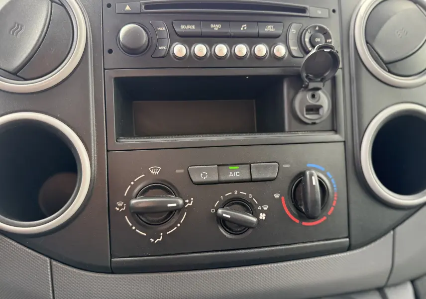 Vue rapprochée du tableau de bord du Peugeot Partner blanc 2017, montrant les commandes de climatisation et la radio.