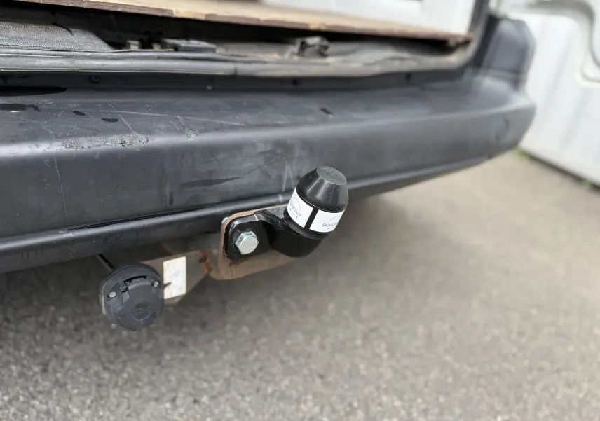 Gros plan sur l'attelage noir fixé au pare-chocs arrière d'un Peugeot Partner blanc de 2017.