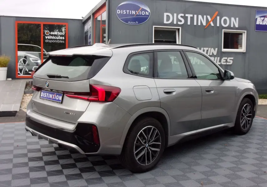 Vue 3/4 arrière droite d’un BMW X1 2024 argent métallisé avec jantes alliage et détails noirs M Sport visibles.