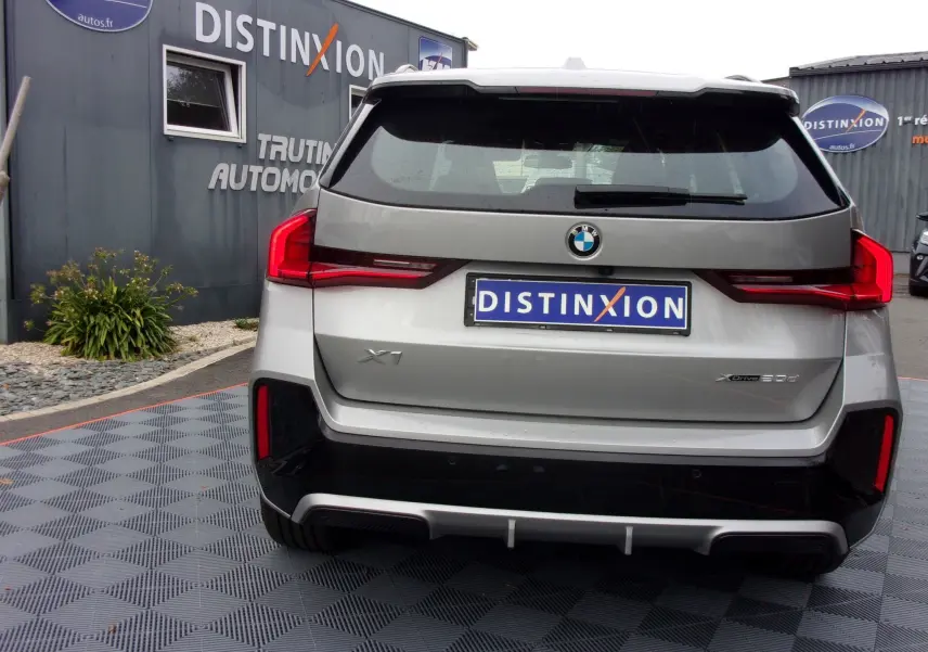 Vue arrière d’un BMW X1 argent métallisé 2024 avec feux arrière LED et logo distinctif sur un parking extérieur.