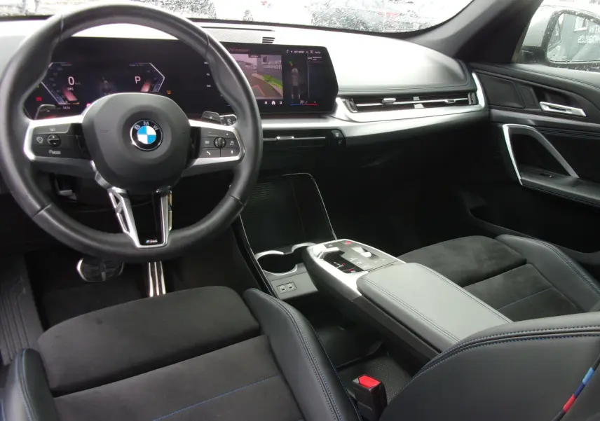 Vue intérieure du poste de conduite du BMW X1 2024 M Sport, avec volant cuir noir et écran central tactile moderne.