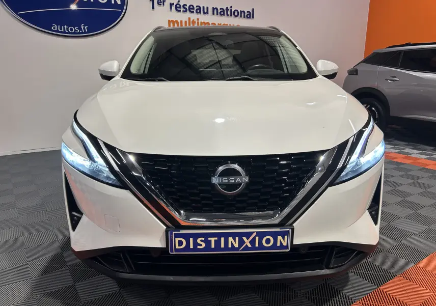 Vue avant d'un Nissan Qashqai blanc lunaire 2023 avec phares LED allumés et calandre noire brillante.