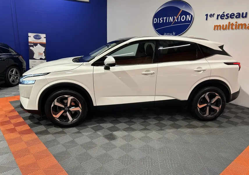 Profil côté gauche du Nissan Qashqai blanc lunaire 2023 en version 1.3 Hybrid N-Connecta, présenté en intérieur showroom.