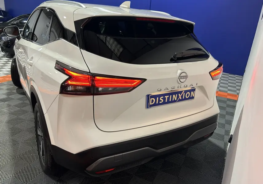 Vue 3/4 arrière droite du Nissan Qashqai blanc lunaire 2023 avec feux arrière allumés et toit panoramique visible.