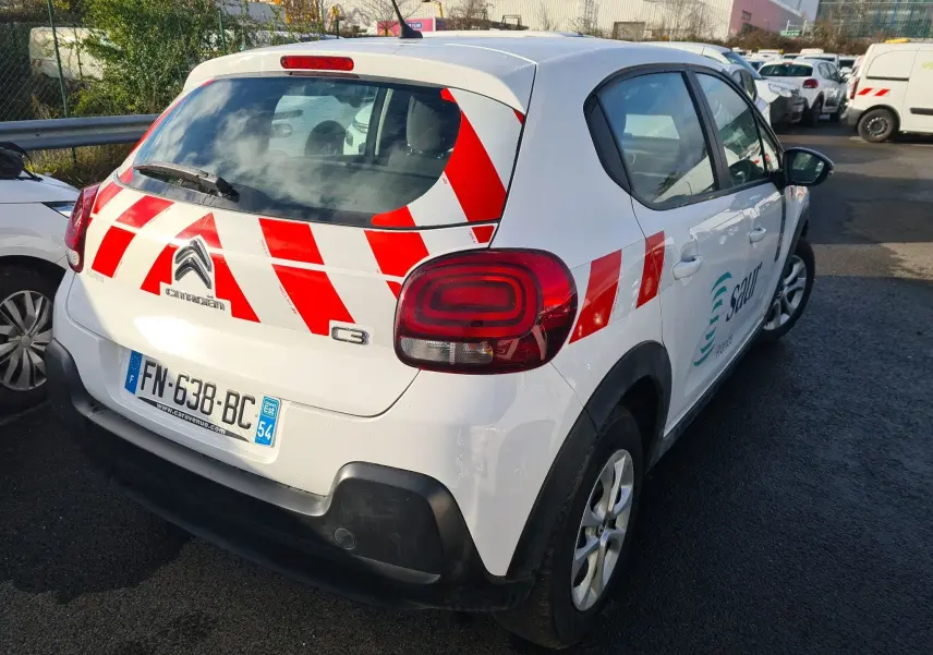 Vue 3/4 arrière droite d'une Citroën C3 blanche 2020 avec bandes rouges diagonales et logo d'entreprise sur la portière.