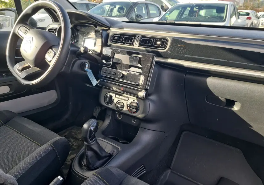 Vue intérieure côté conducteur de la Citroën C3 Société blanche de 2020, avec tableau de bord noir et levier de vitesses manuel.