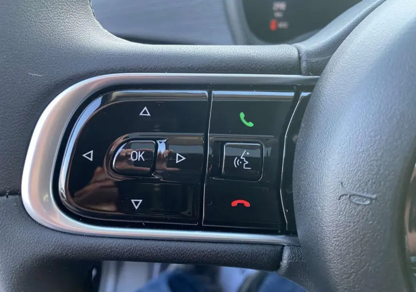 Gros plan sur les commandes du volant côté gauche de la Fiat 500 électrique noire, avec boutons de téléphone et navigation.
