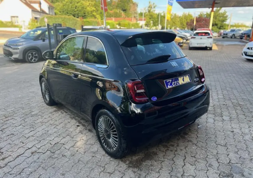 Vue 3/4 arrière droite d'une FIAT 500 électrique noire avec jantes stylisées et poignées de portes dissimulées.