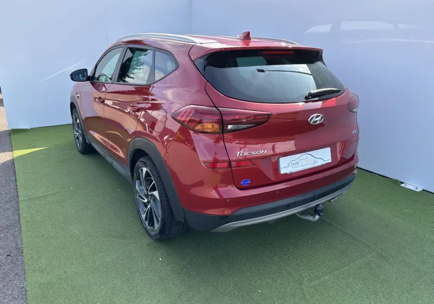 Vue 3/4 arrière droite d'un Hyundai Tucson rouge métallisé avec attelage et jantes alliage 17 pouces.