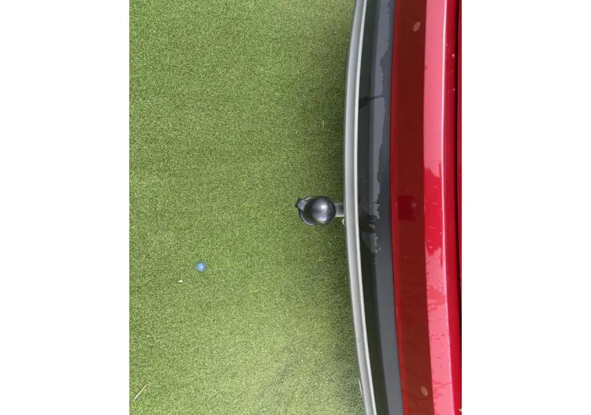 Vue rapprochée de l'arrière droit d'un Hyundai Tucson rouge métallisé avec attelage sur fond d'herbe synthétique.